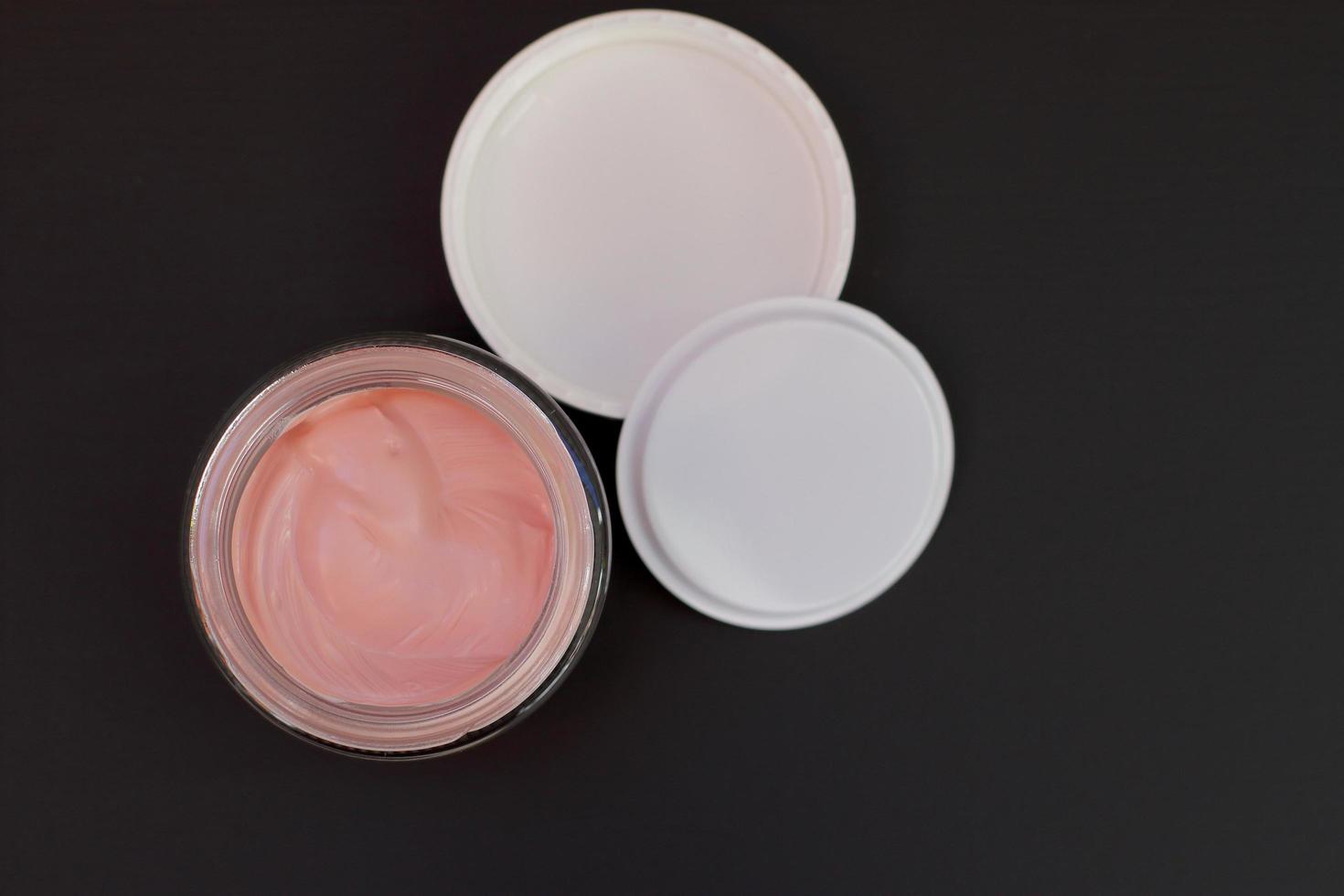 Pink cosmetic clay in glass jar, black background, isolated photo