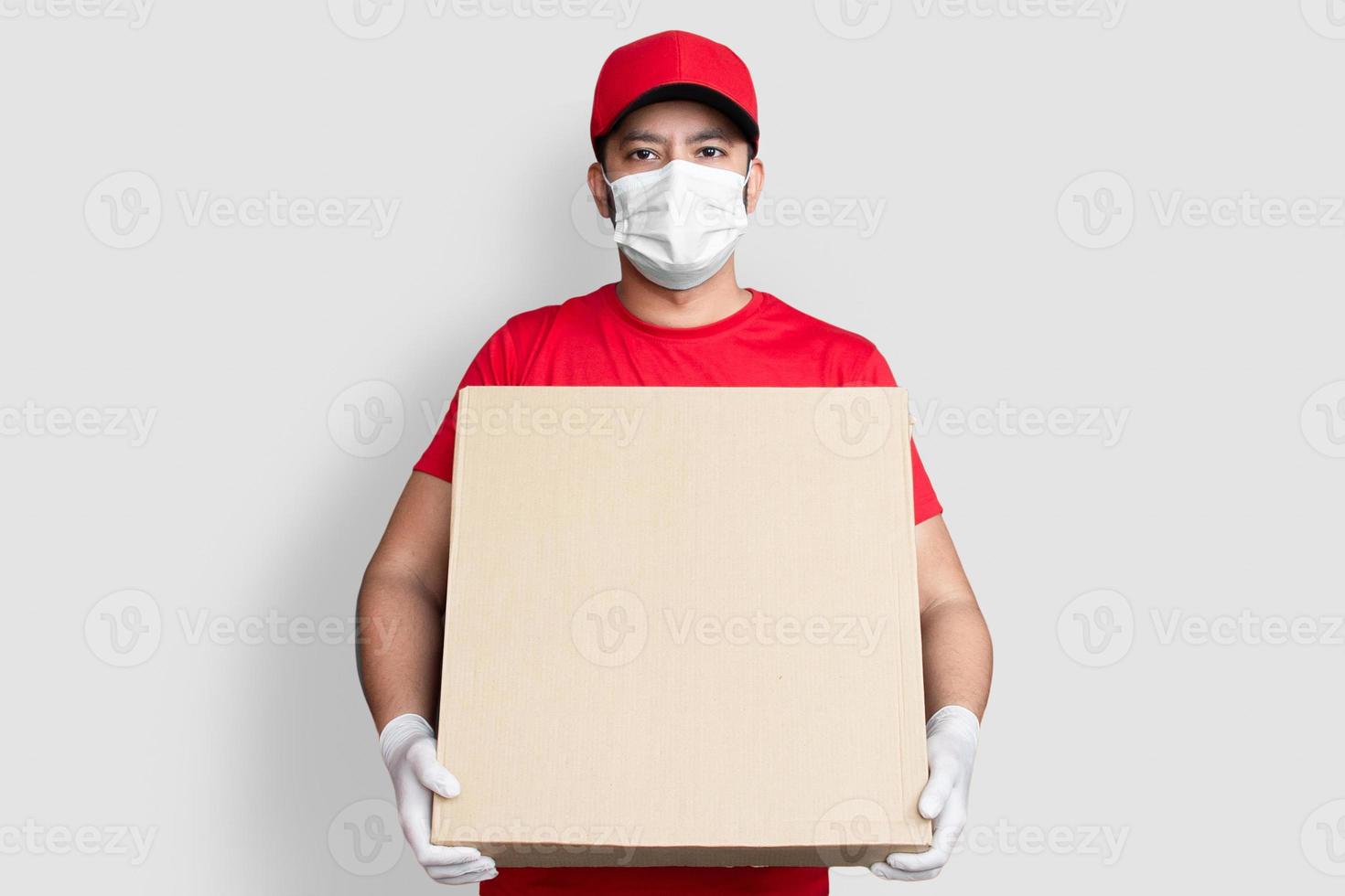 Repartidor empleado en gorra roja camiseta en blanco uniforme mascarilla mantenga caja de cartón vacía aislada sobre fondo blanco foto