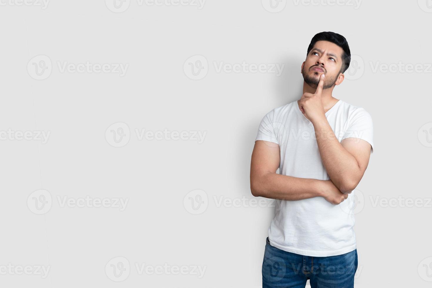 Asian handsome man on white t-shirt having doubts while looking up over isolated white background photo