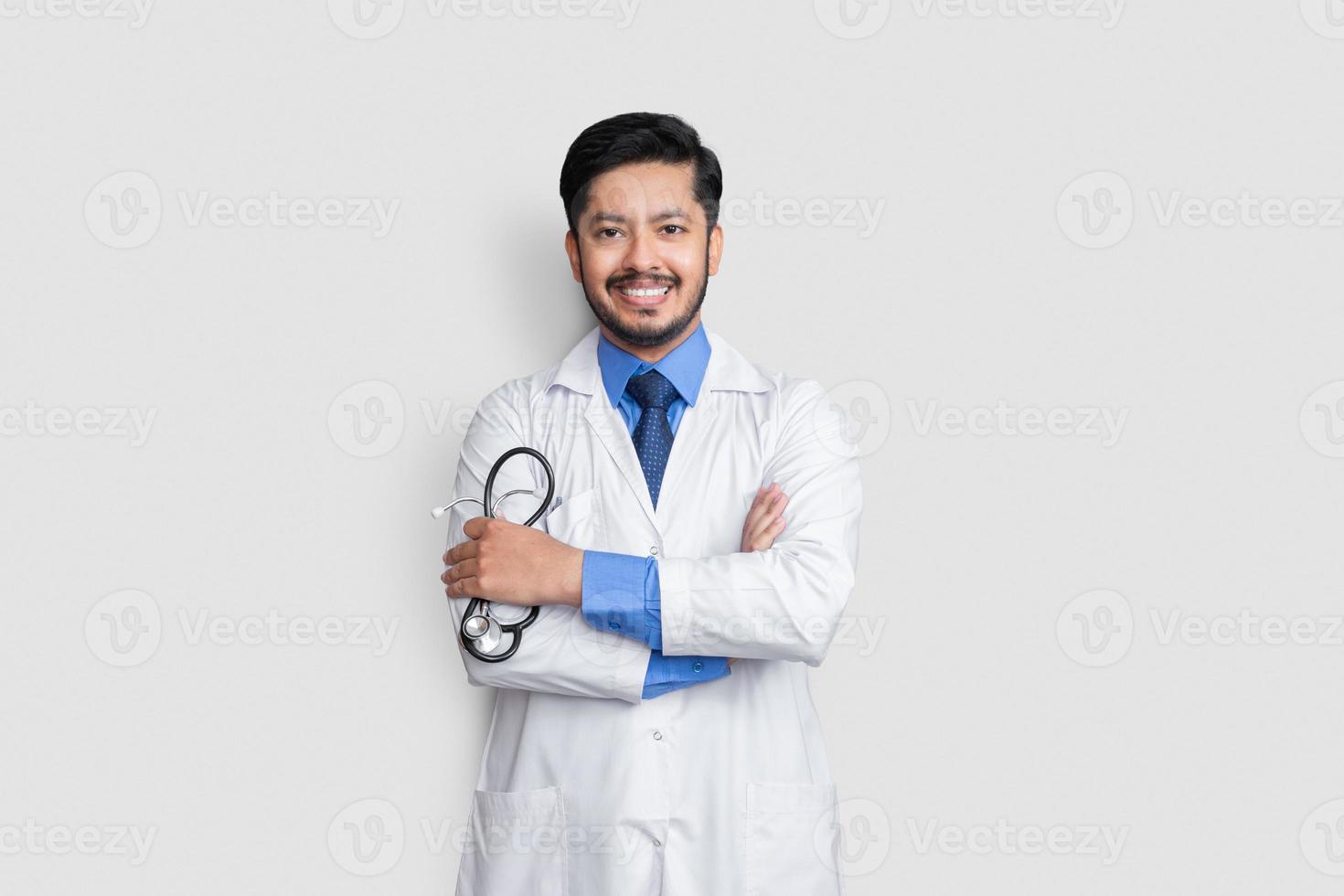 Joven médico varón de brazos cruzados sobre fondo aislado sonriendo foto