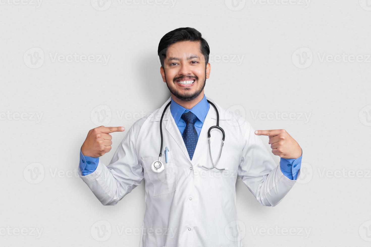 Handsome Pakistani doctor and stethoscope looking confident with smile on face, pointing oneself with fingers proud and happy. photo