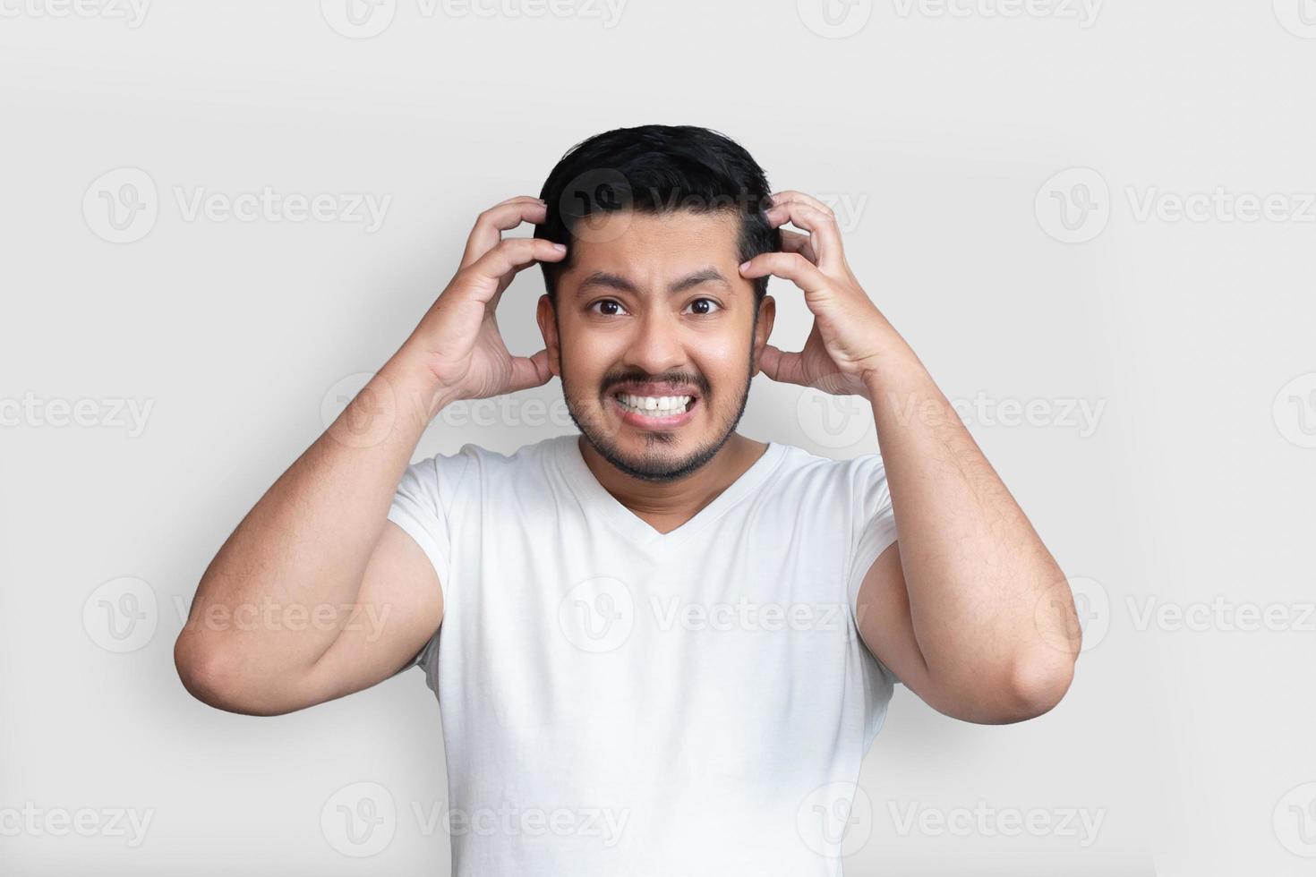 Cerrar la foto del hombre joven con los brazos de apariencia perfecta con las manos en la frente. Dolor terrible en los ojos, camiseta blanca casual de uso cerrado aislado en el fondo