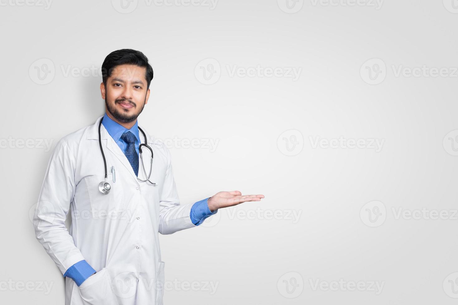 Doctor vistiendo uniforme sonriendo mientras presenta y apunta aislado sobre fondo blanco con espacio de copia foto