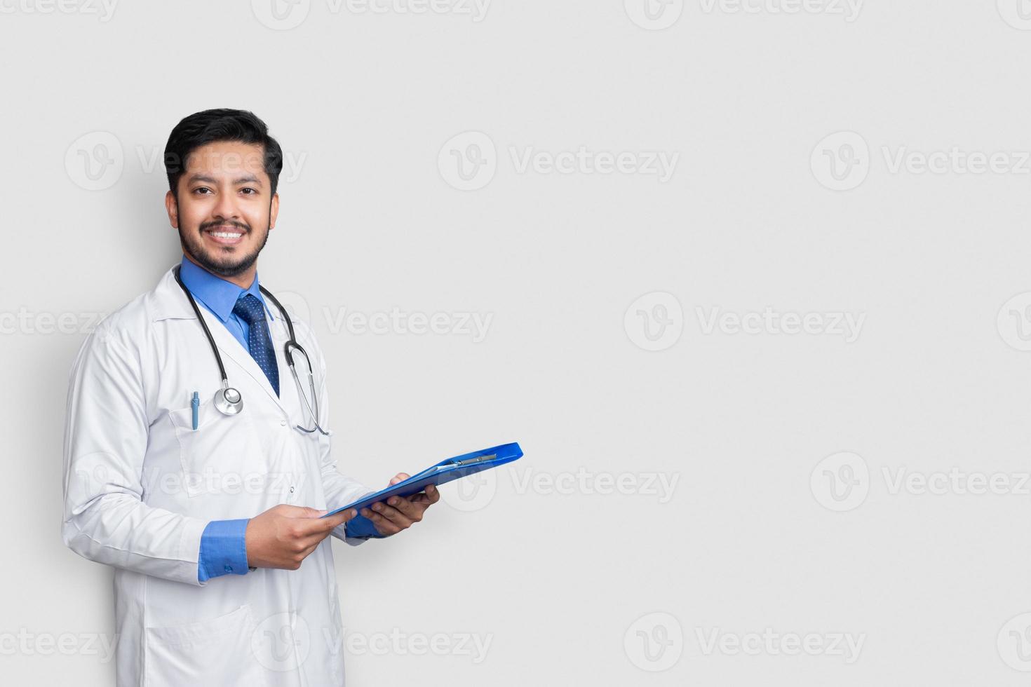 Doctor en bata de laboratorio sosteniendo el expediente del paciente o registro médico mirando a la cámara, aislado sobre fondo blanco. foto