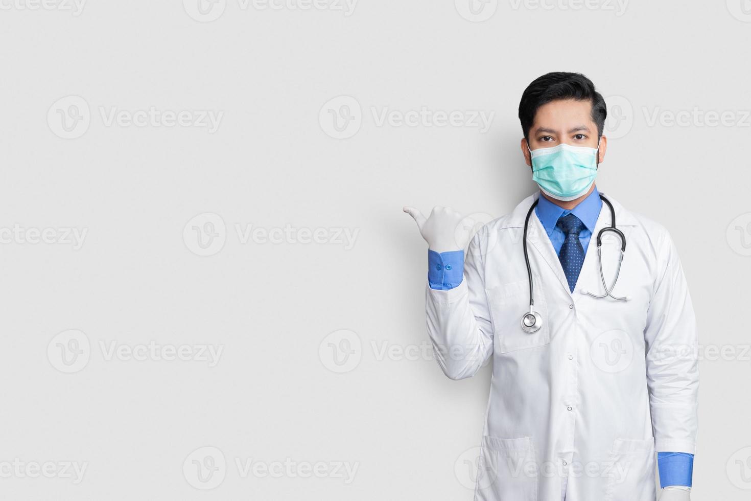 Doctor vistiendo uniforme de máscara sonriendo mientras presenta y apunta aislado sobre fondo blanco con espacio de copia foto