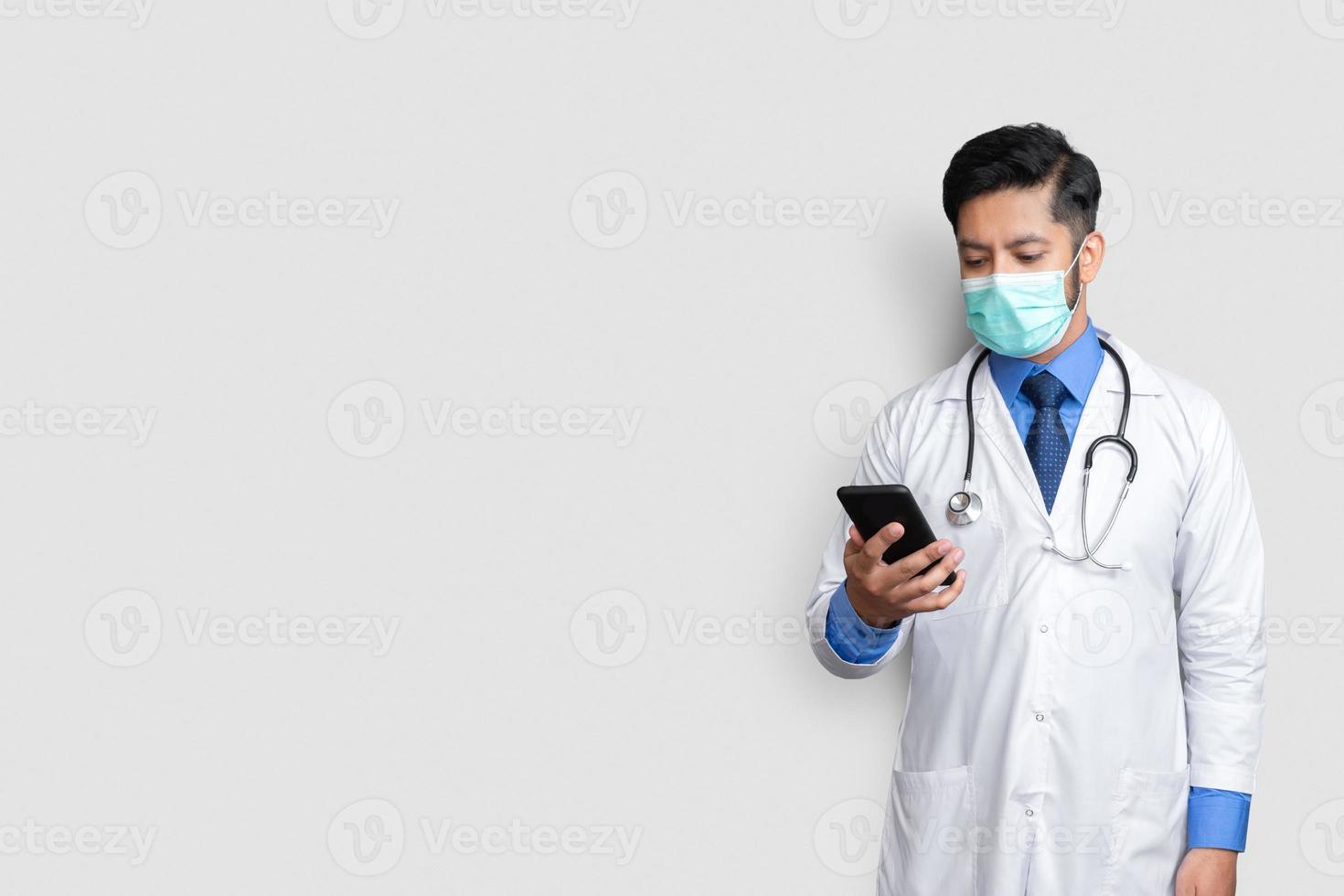 médico con máscara mirando el teléfono. Medicina de tecnología médico paquistaní en casa espacio de copia foto