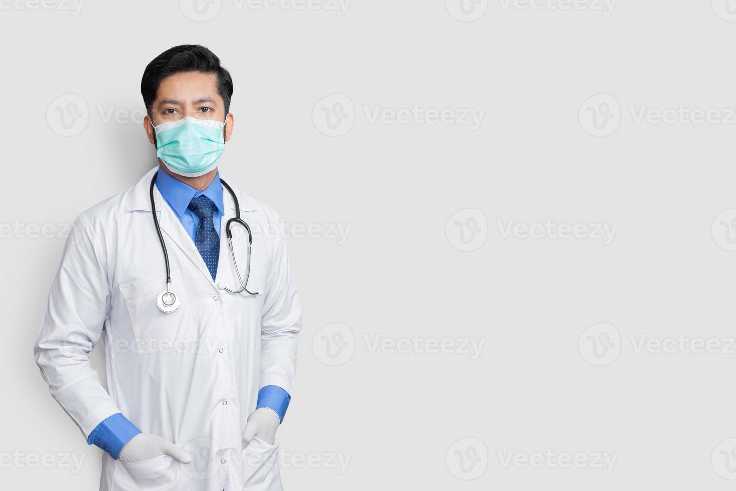 Young male doctor face covered with mask and arm in coat over isolated background photo