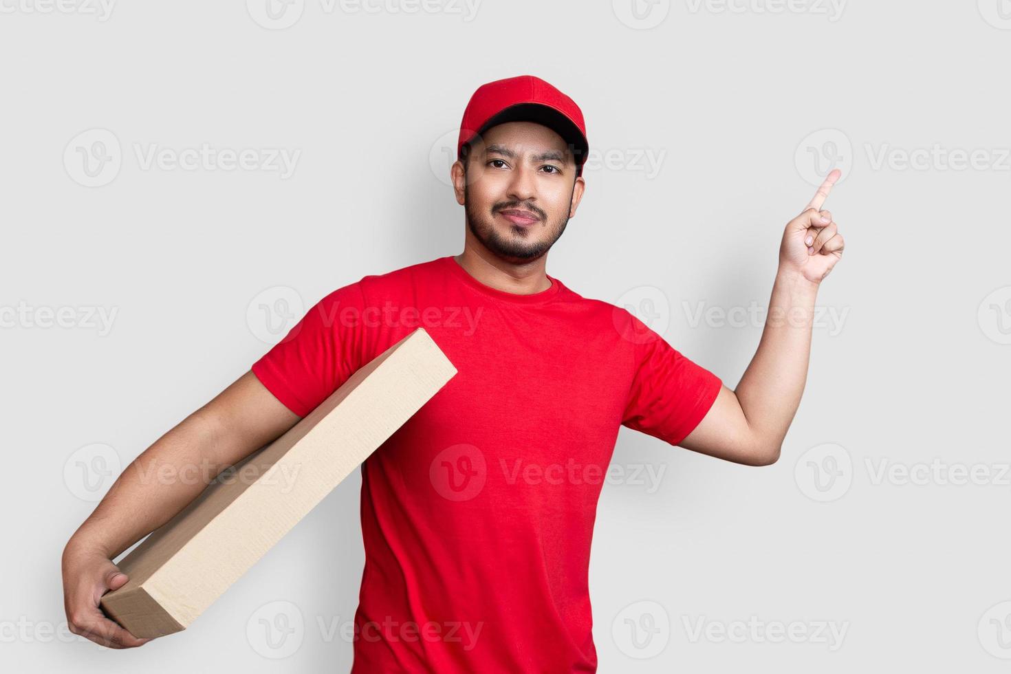 Delivery man employee in red cap blank t-shirt finger uniform hold empty cardboard box isolated on white background photo