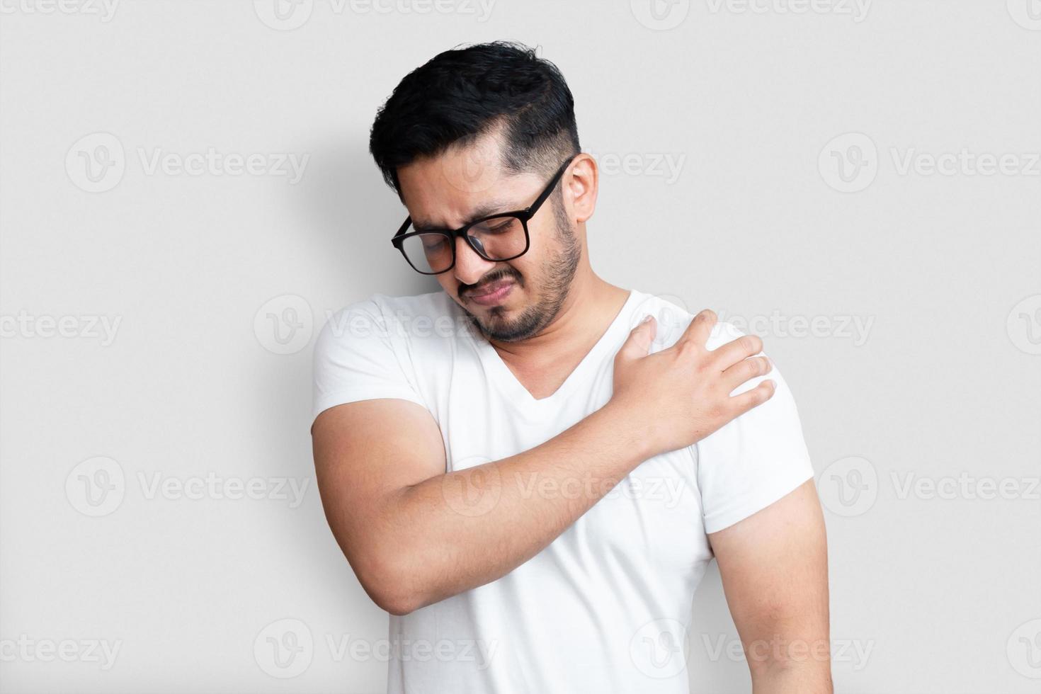 Apuesto joven con gafas negras con dolor en el hombro sobre fondo blanco. foto