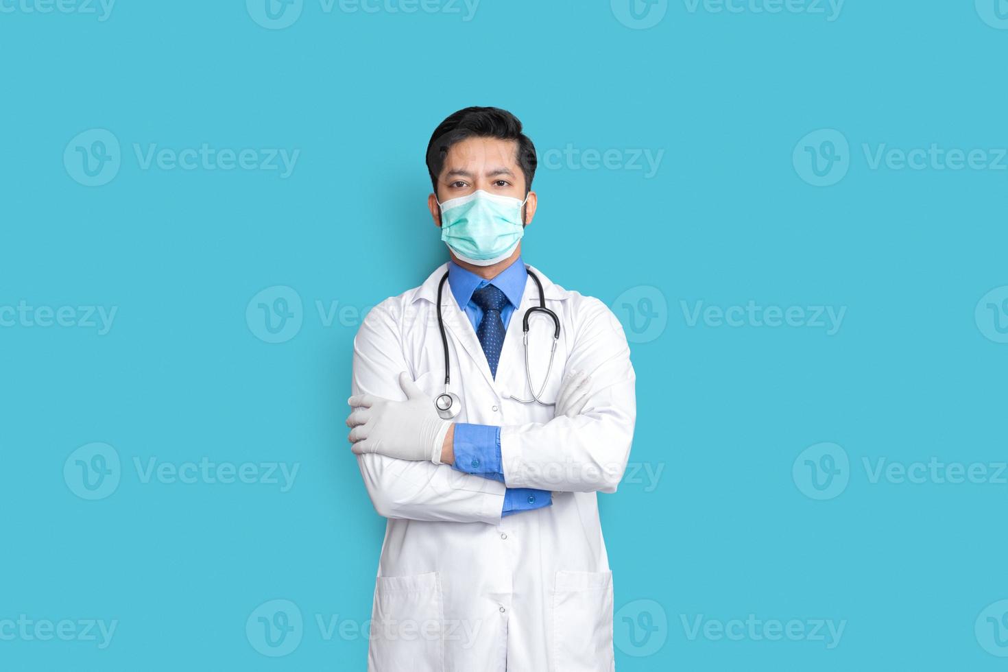 Young male doctor face covered with mask and arm cross over isolated background photo