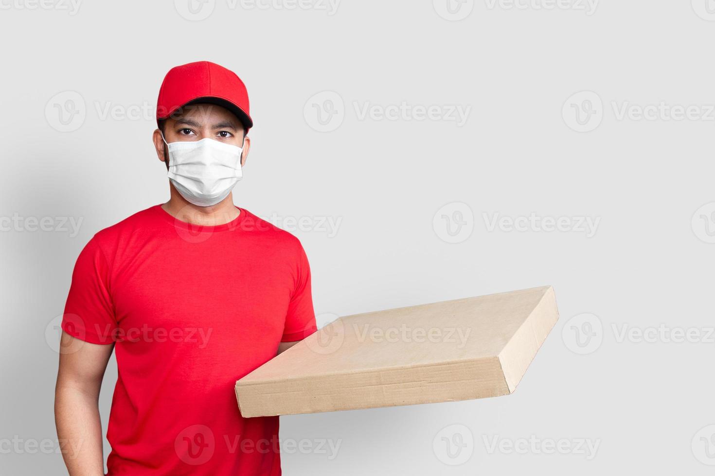 Repartidor empleado en gorra roja camiseta en blanco uniforme mascarilla mantenga caja de cartón vacía aislada sobre fondo blanco foto