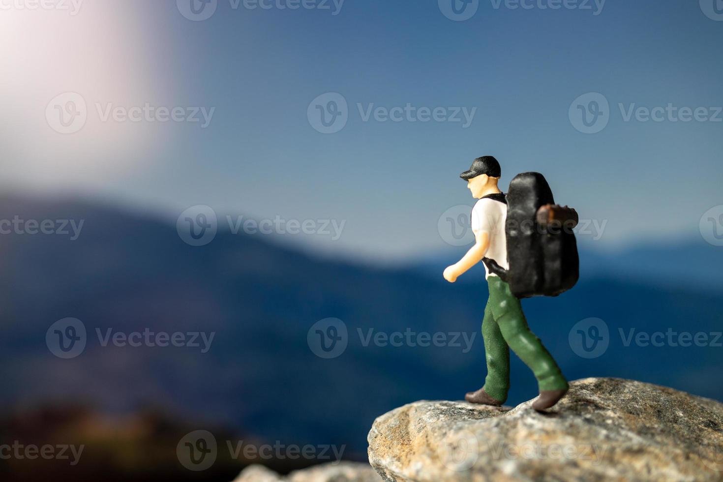 Viajero de personas en miniatura con mochila caminando sobre la roca foto