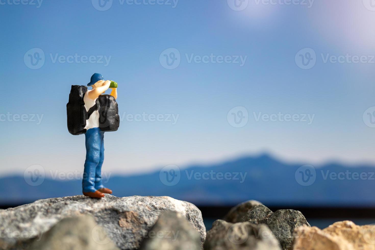 Viajero de personas en miniatura con mochila caminando sobre la roca foto