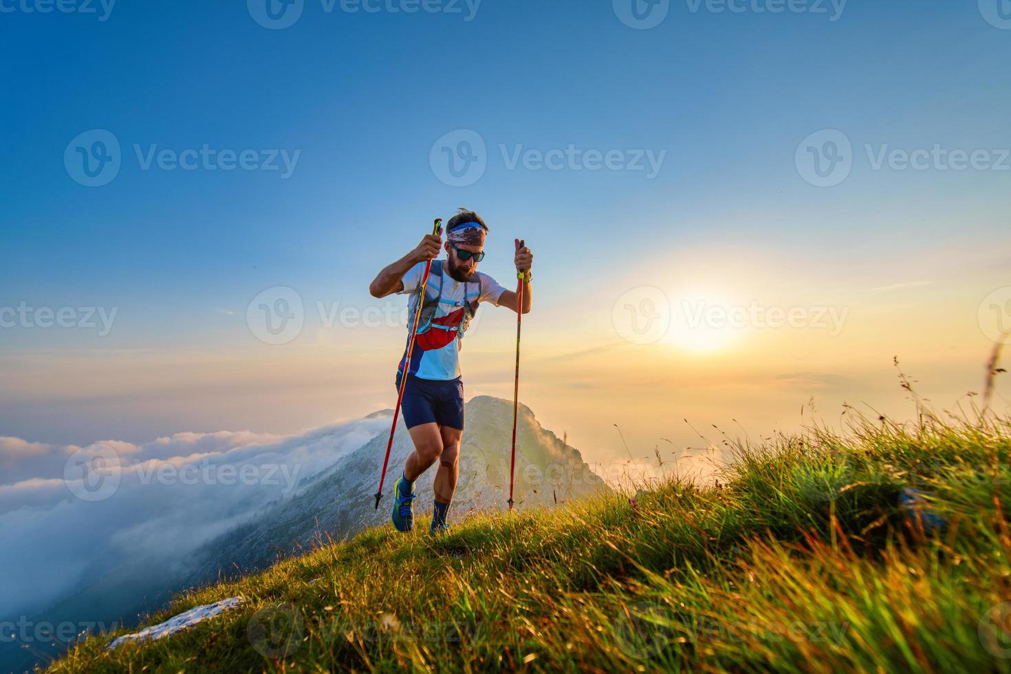 hombre con postes en las montañas con puesta de sol detrás foto