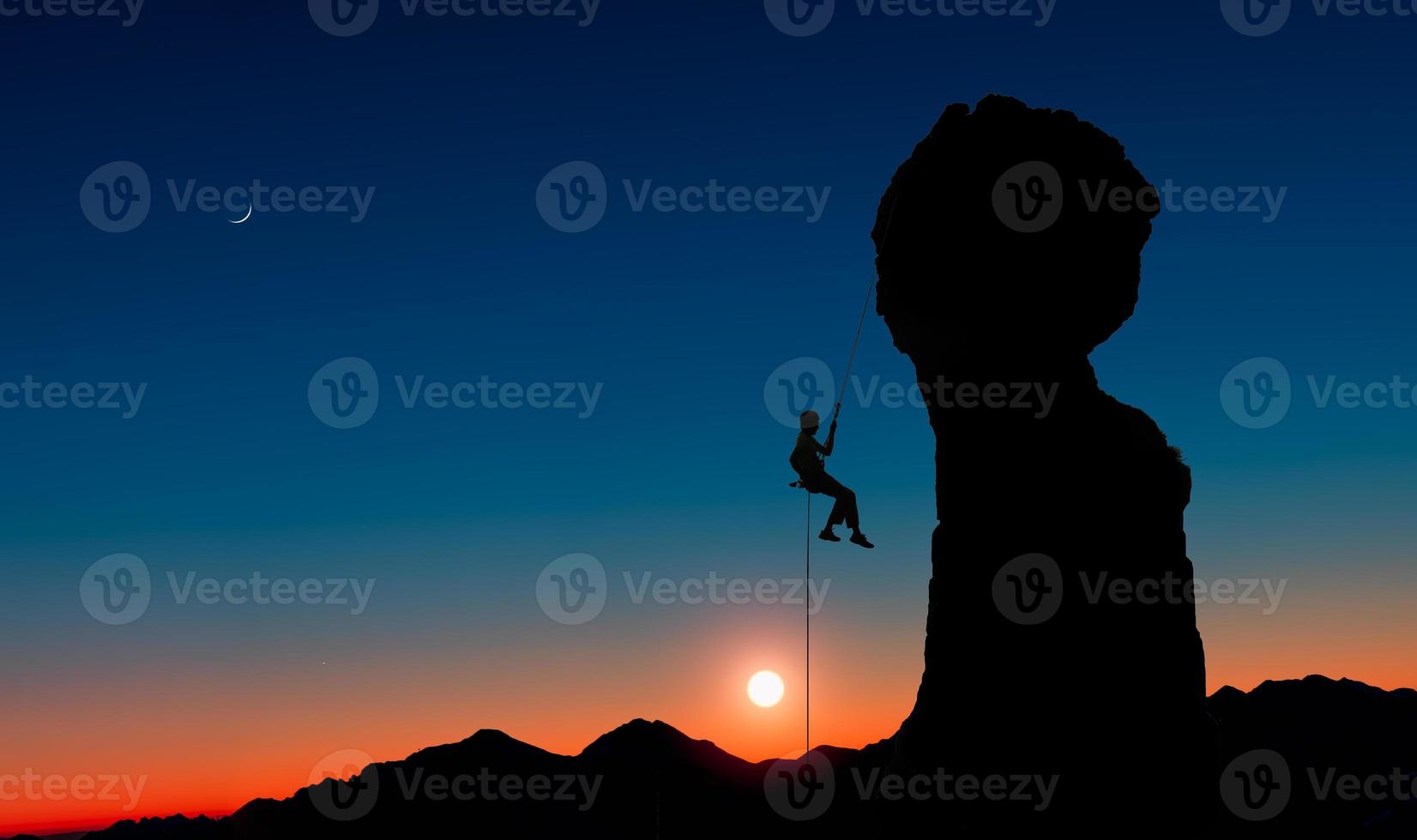 Un escalador haciendo rappel desde un pico rocoso al atardecer foto