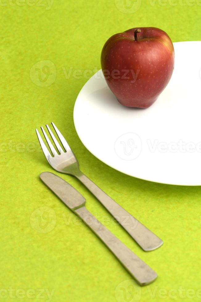 Delicious apple in plate with knife and fork on green background photo