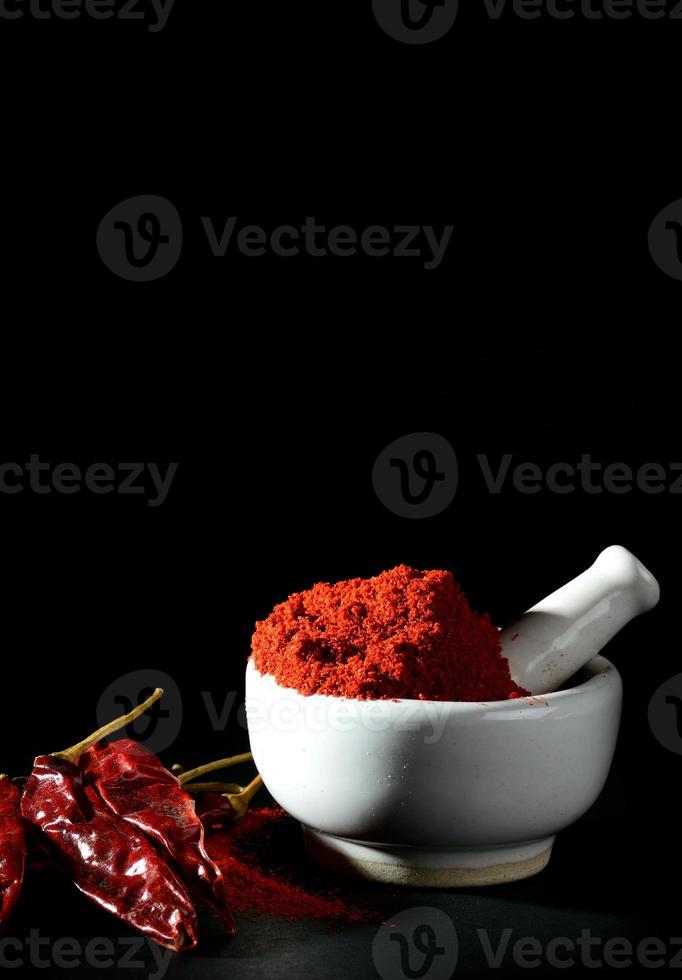 Red Chili Pepper powder in pestle with mortar and Red Chili Peppers on black background photo