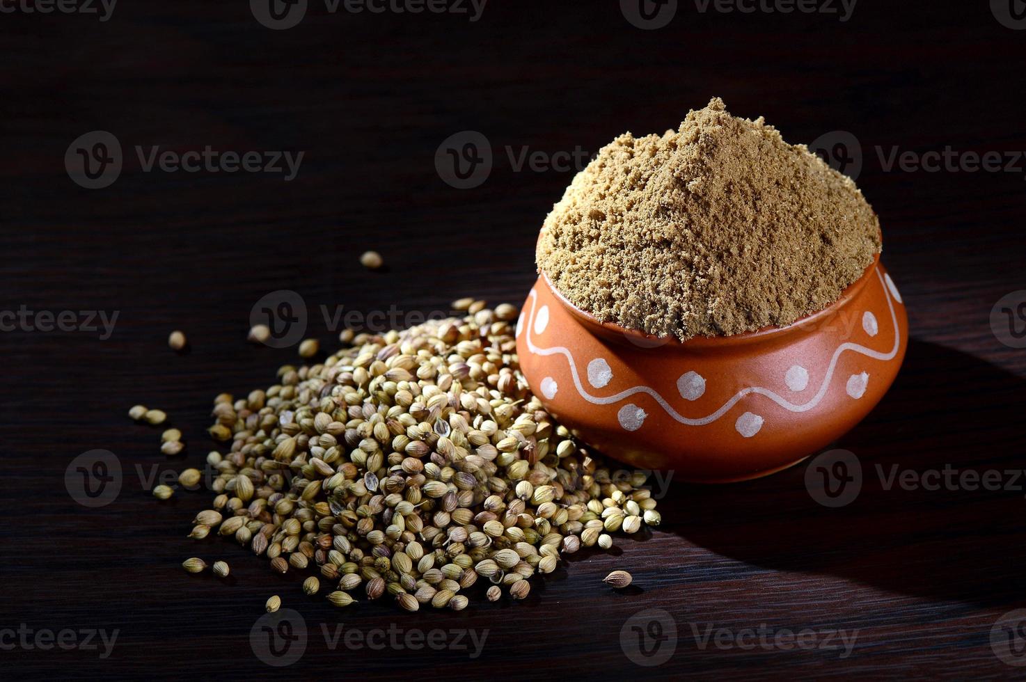 Coriander seeds and Powdered coriander in clay pot on wooden background. photo