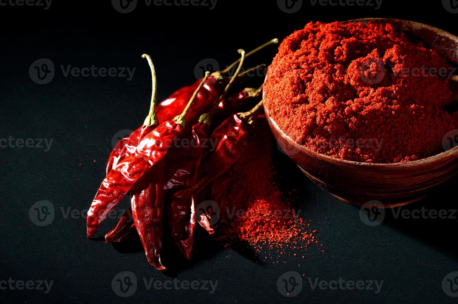 Polvo frío en un tazón de madera con chiles rojos secos y fríos sobre fondo negro foto