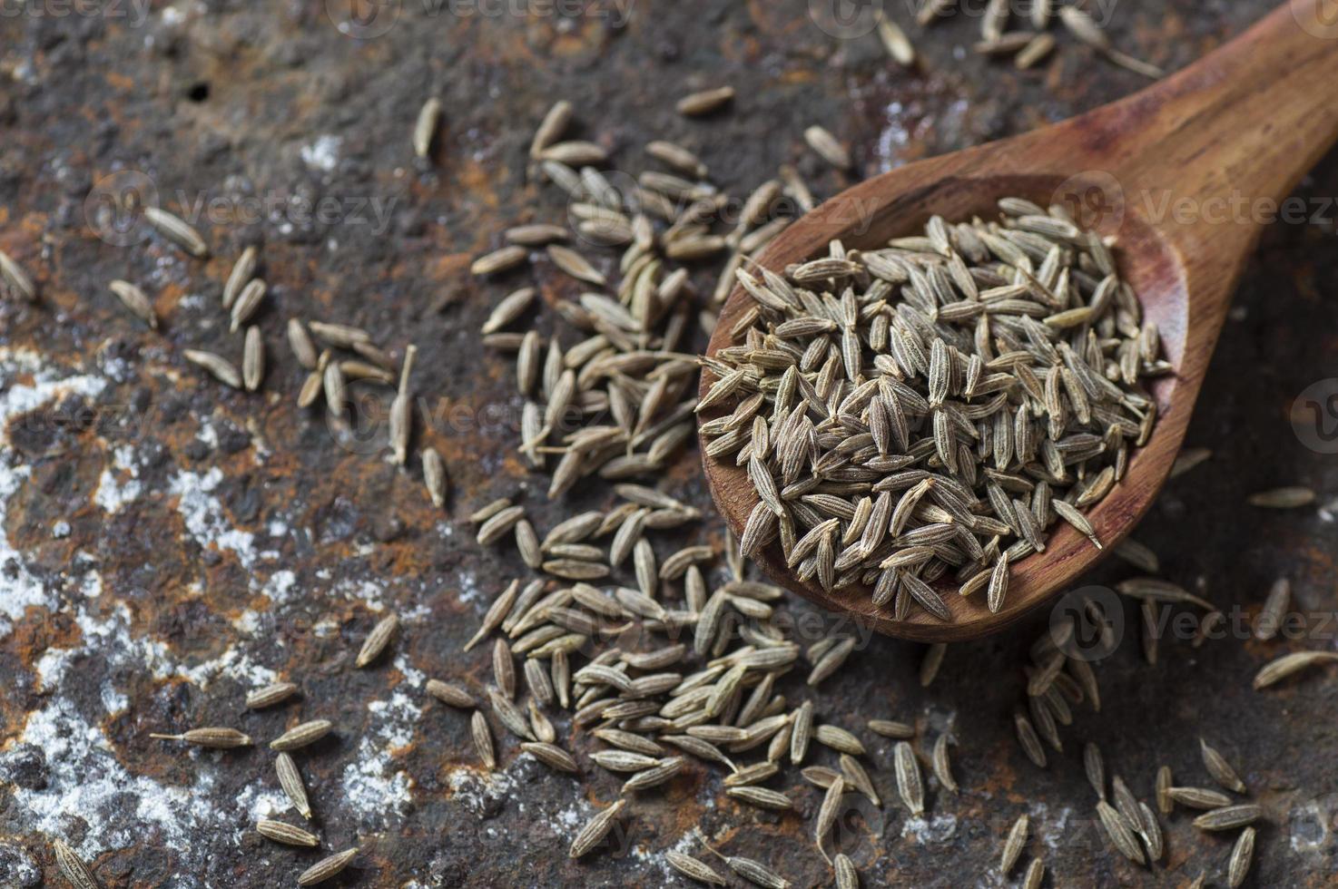 Semillas de comino en una cuchara de madera sobre un fondo de textura foto