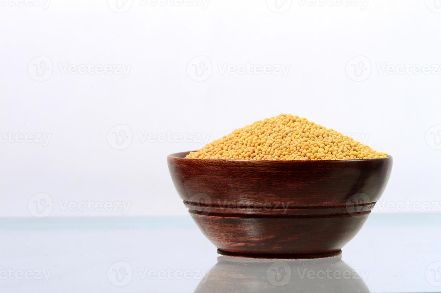 yellow mustard seeds in wooden bowl isolated on white background photo