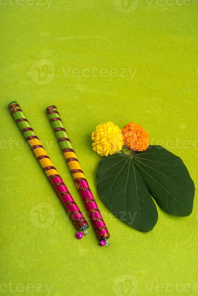 Indian Festival Dussehra and Navratri, showing golden leaf Bauhinia racemosa and marigold flowers with Dandiya sticks on a green background photo