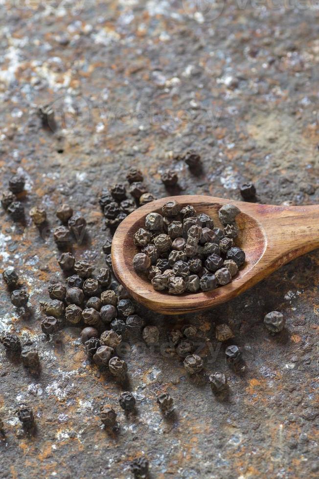 Peppercorns in wooden spoon on texture background photo