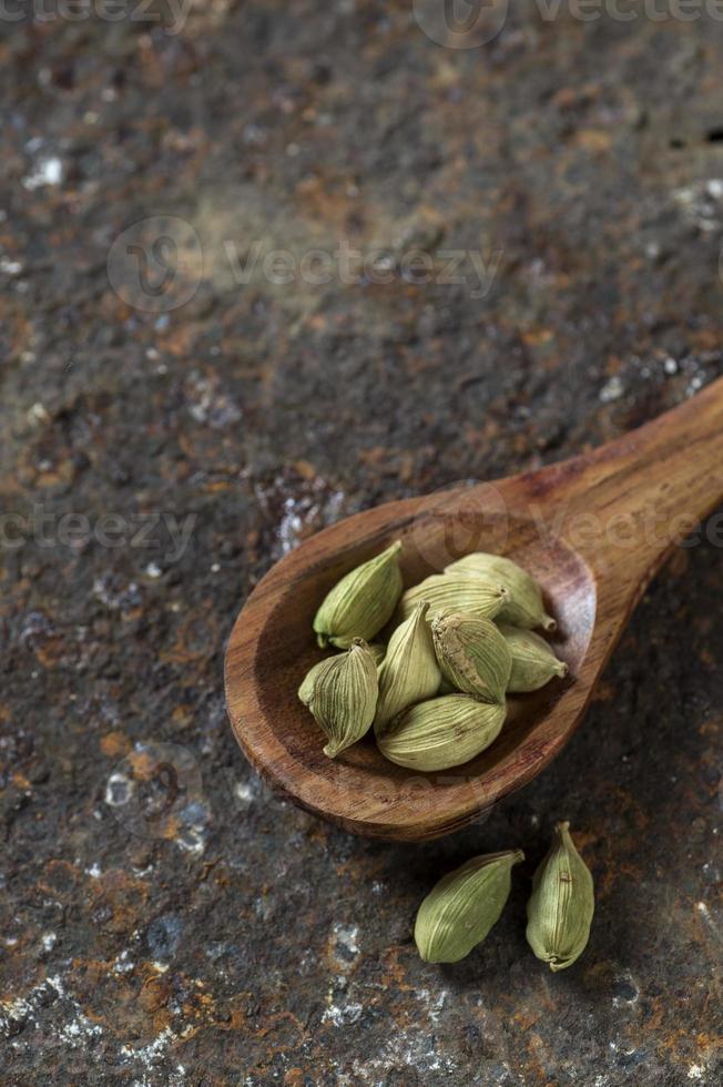 Cardamom pods in wooden spoon on a textured background photo