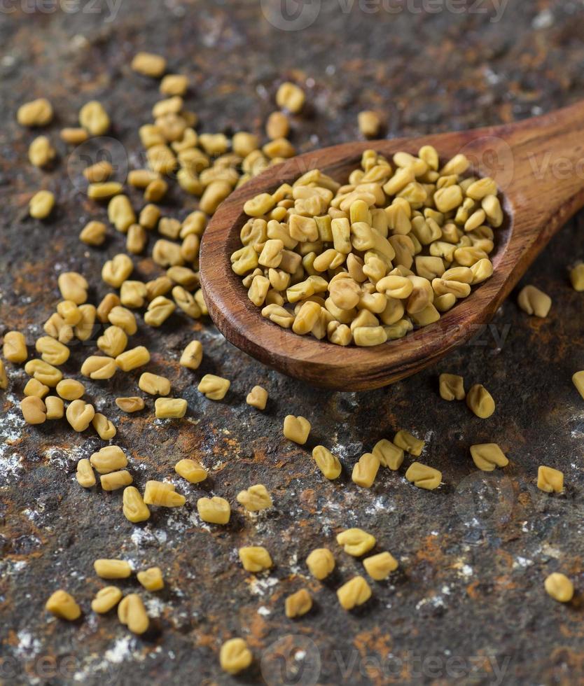 Fenugreek seeds in wooden spoon on textured background photo