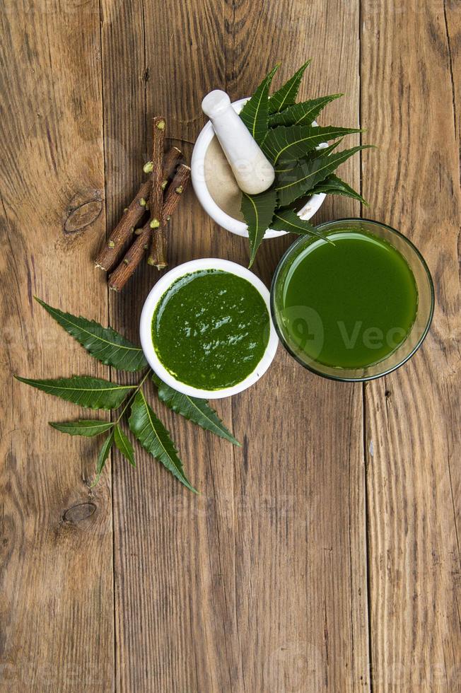 Hojas de neem medicinales en mortero con pasta de neem, jugo y ramitas sobre fondo de madera foto