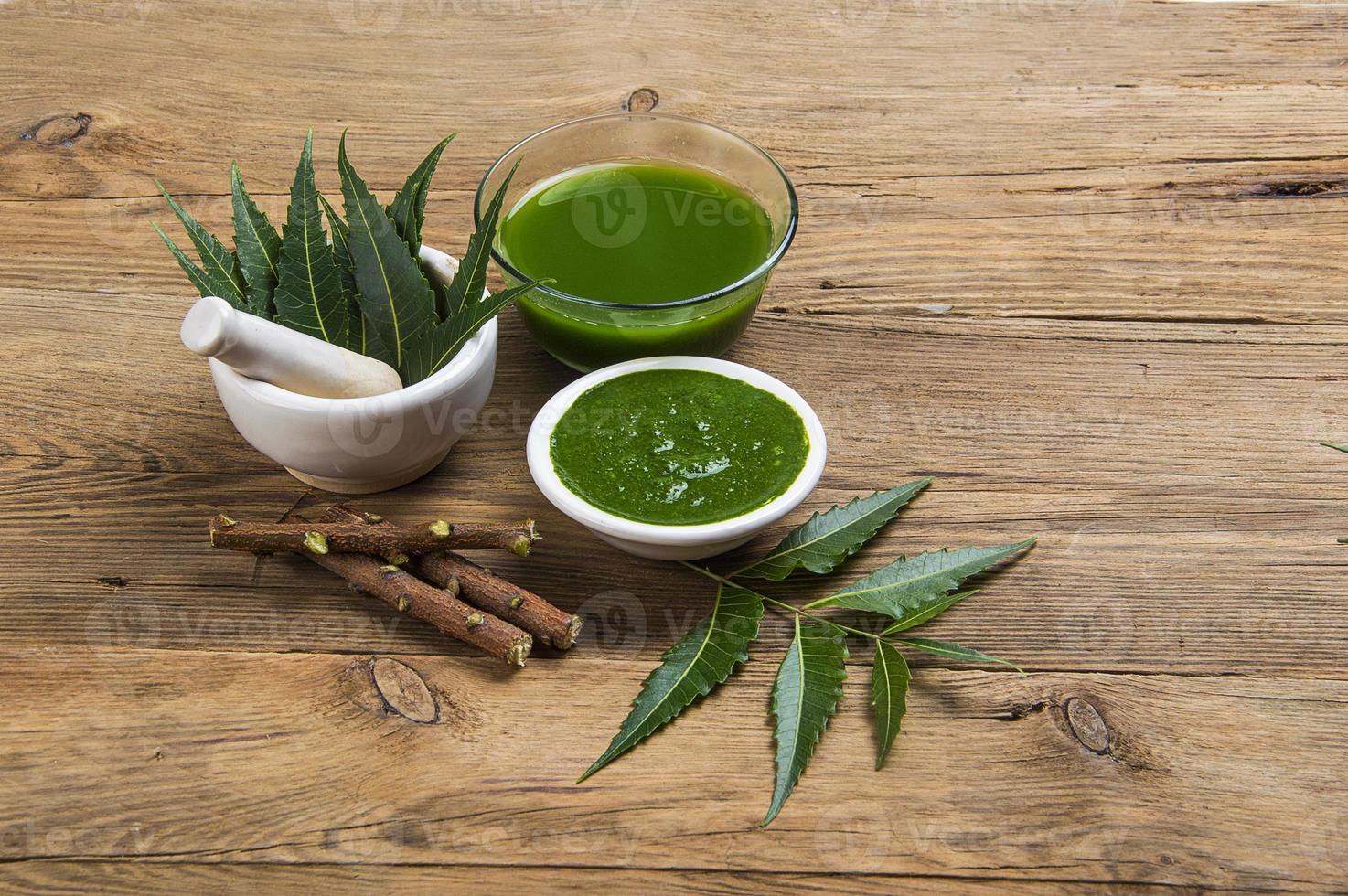 Hojas de neem medicinales en mortero con pasta de neem, jugo y ramitas sobre fondo de madera foto