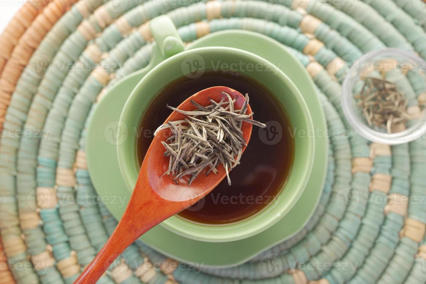 Vista superior del té verde y hojas de hierbas en un pequeño recipiente de vidrio sobre la mesa foto