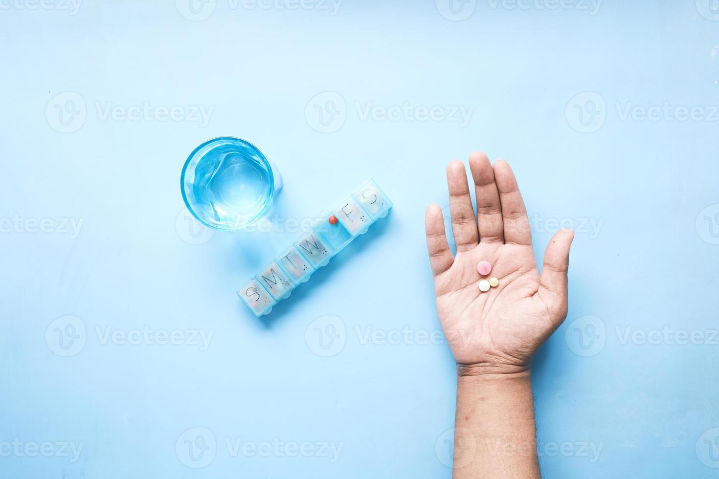 top view of pills on palm of hand with pill box and glass on water on table photo