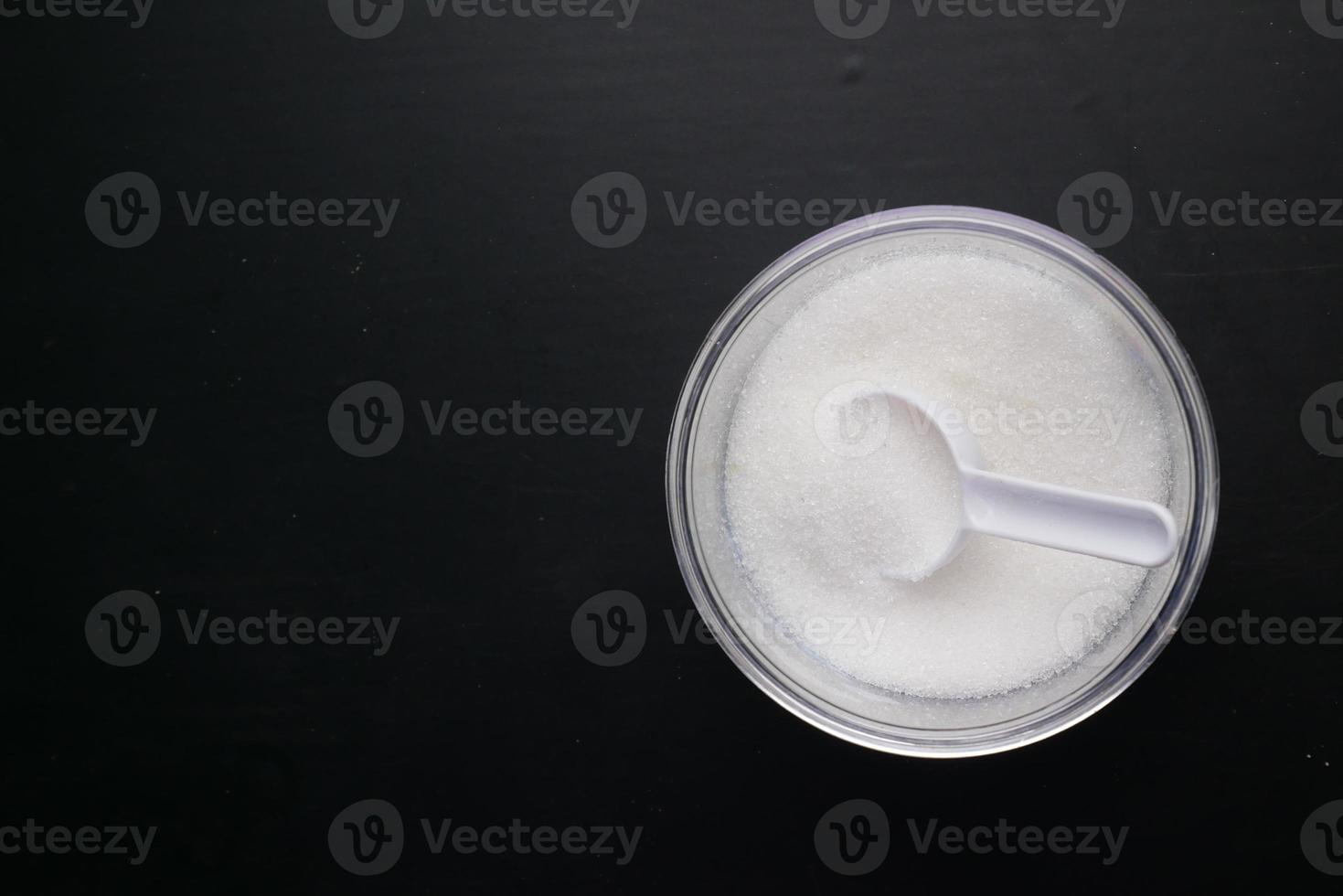 white sugar and spoon in a container on black background, photo