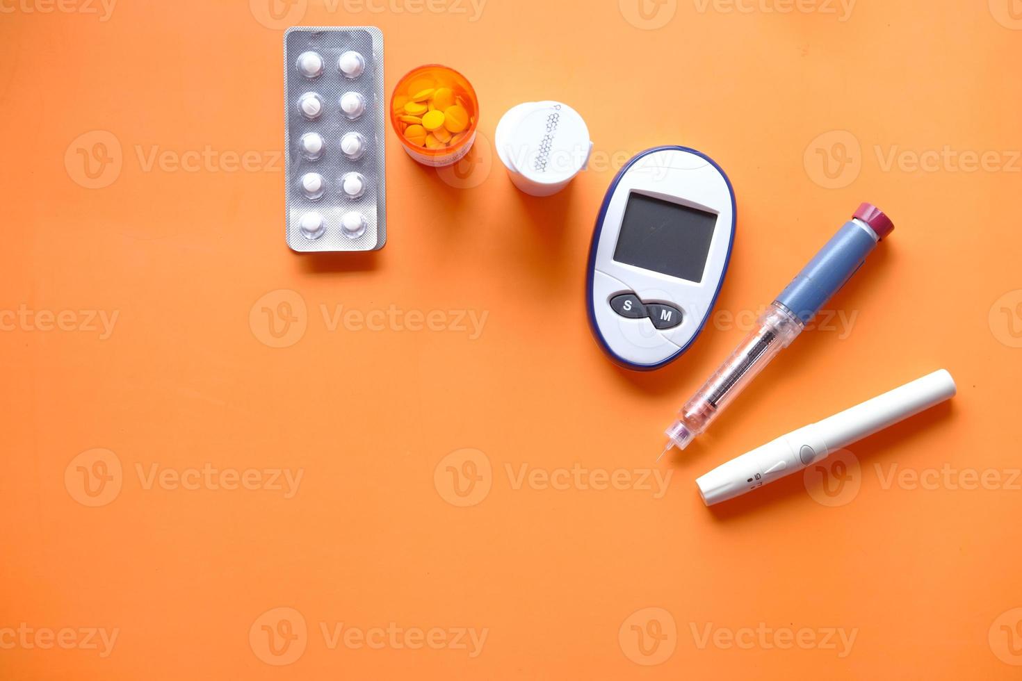 insulin pen, diabetic measurement tools and pills on orange background photo