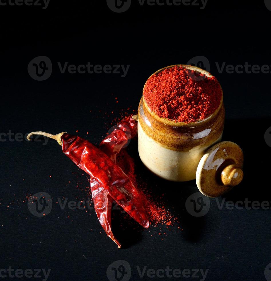 Red Chili Pepper powder in clay pot with Red Chili Peppers on black background photo