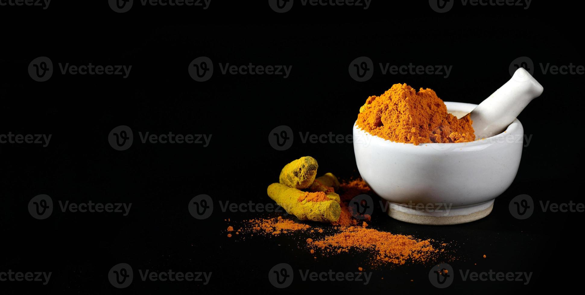 Turmeric powder in mortar with pestle and roots or barks on black background photo