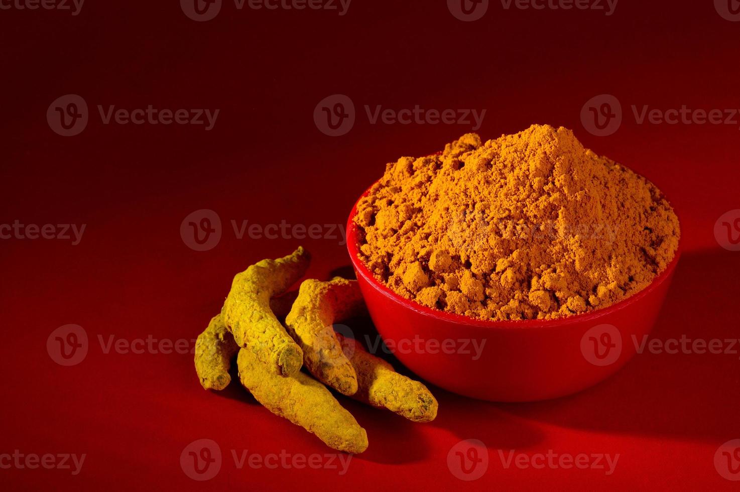 Cúrcuma seca en polvo y raíces o cortezas en un tazón rojo sobre fondo rojo. foto