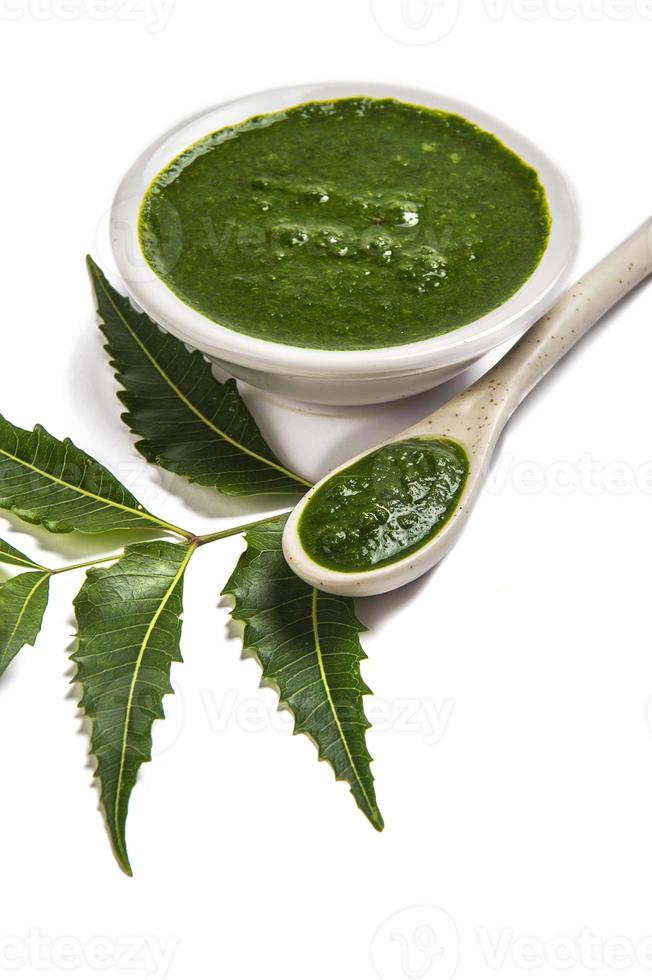 Hojas de neem medicinales con pasta de neem en cuchara y plato sobre fondo blanco. foto