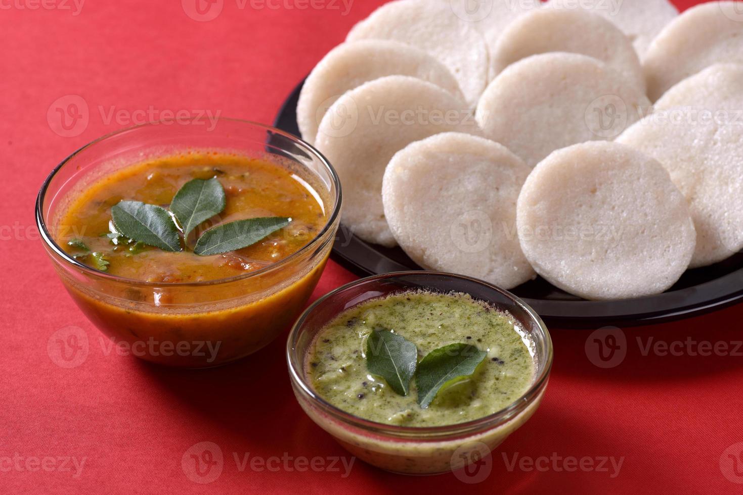 idli con sambar y chutney de coco sobre fondo rojo, plato indio, comida favorita del sur de la India, rava idli o sémola sin hacer nada o rava sin hacer nada, servido con sambar y salsa picante verde. foto