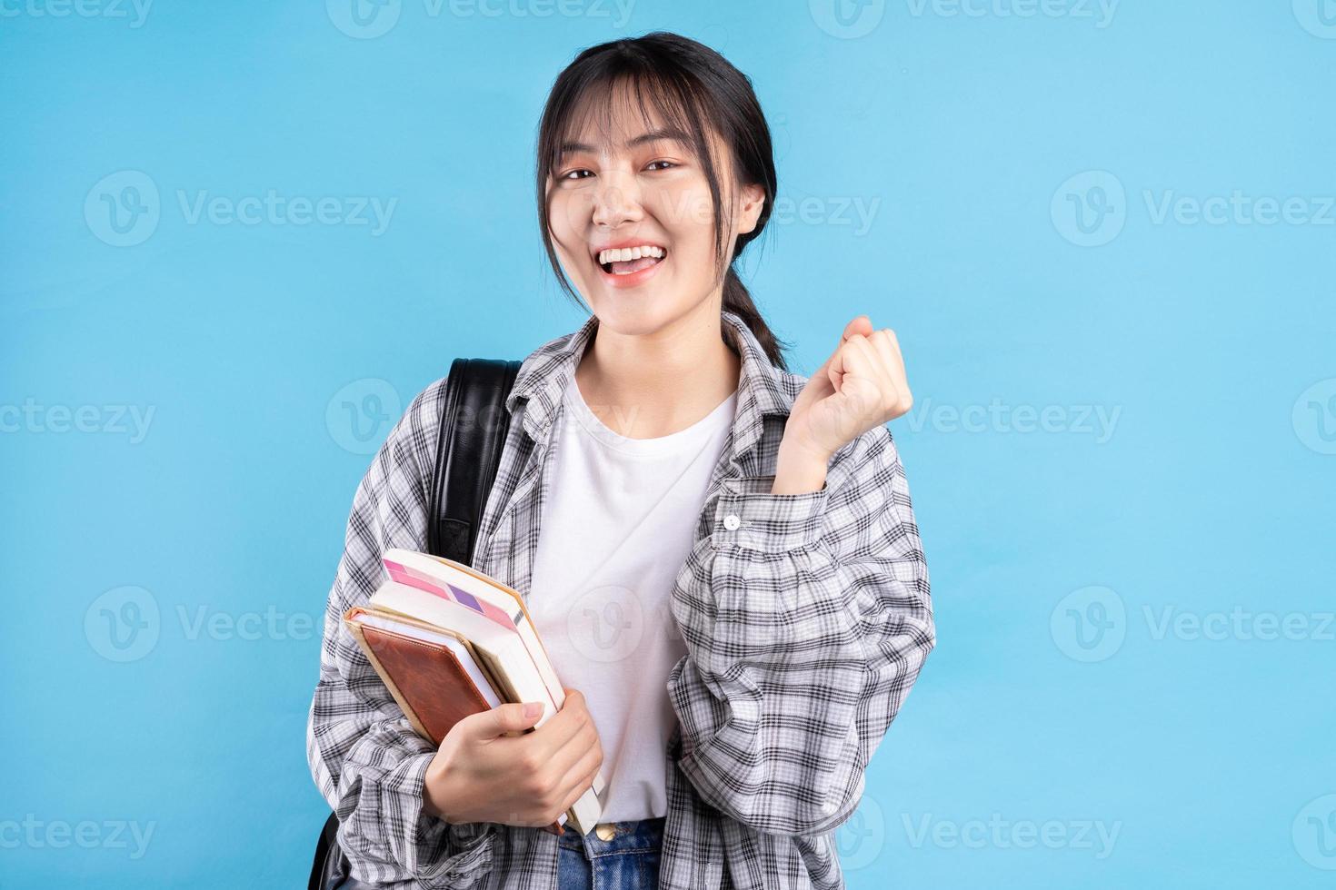 Estudiante asiática con expresión lúdica sobre fondo azul. foto