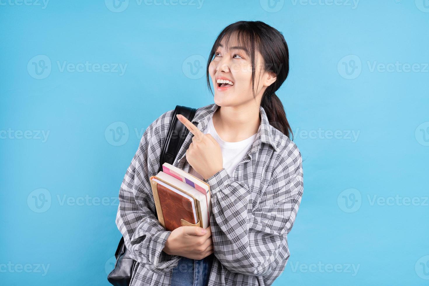Estudiante asiática con expresión lúdica sobre fondo azul. foto