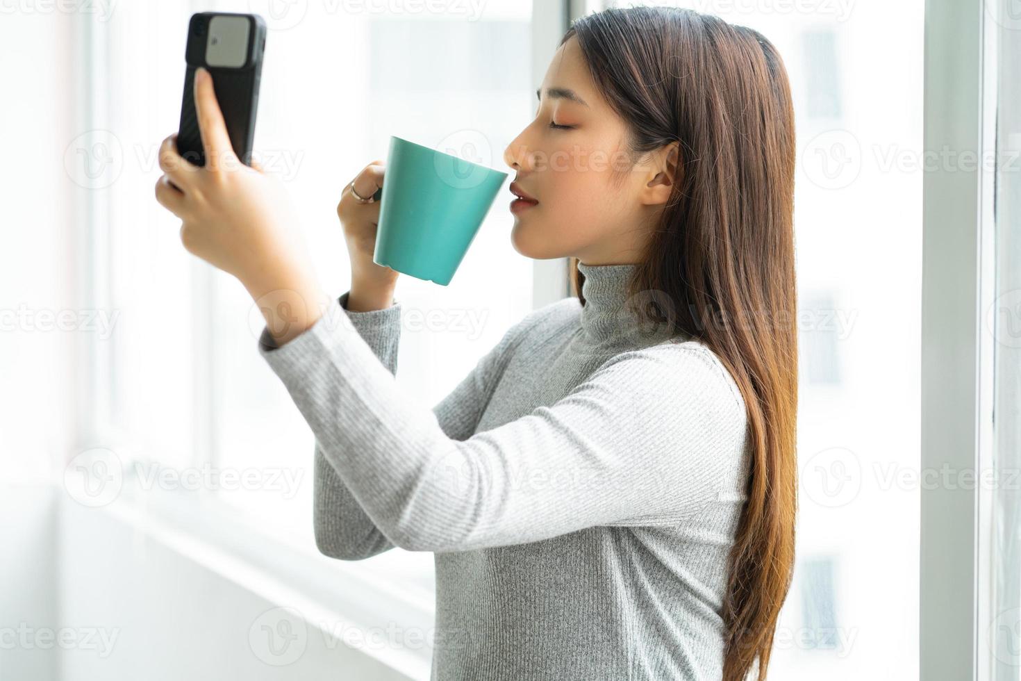 Asian business woman standing taking selfie photo by window