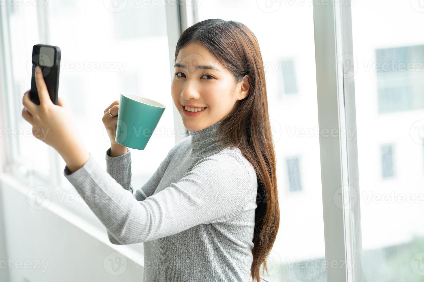 Asian business woman standing taking selfie photo by window.