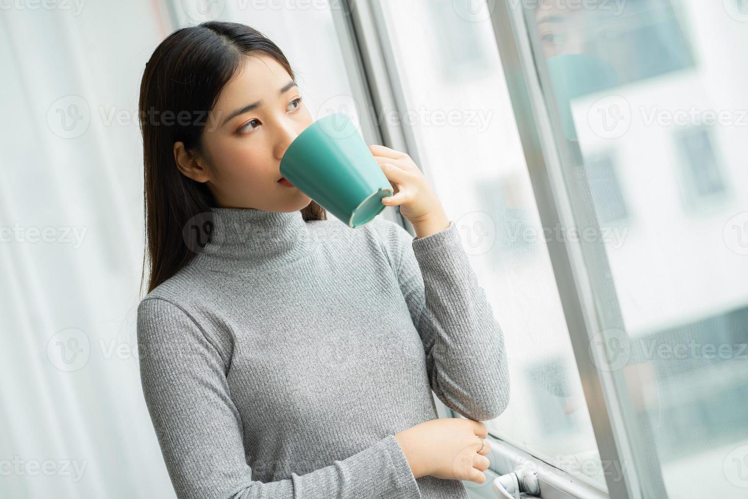 Asian woman drinking coffee by the window during break photo