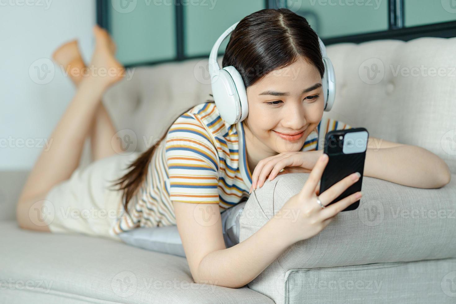 Beautiful Asian woman lying on sofa and listening to music while using phone photo