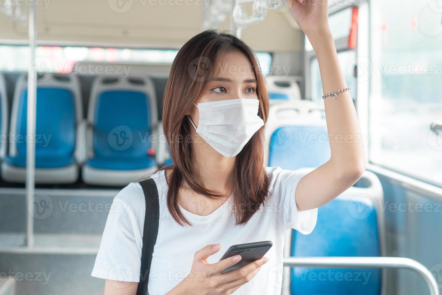 Chica asiática con máscara mientras usa el teléfono inteligente en el autobús foto