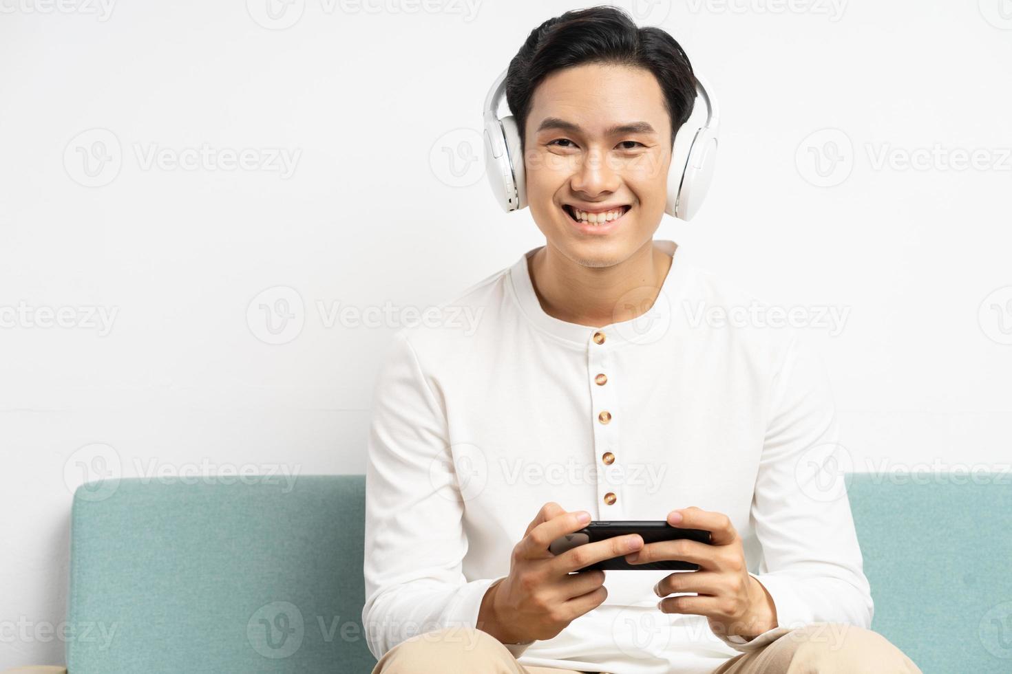 Hombre asiático usando audífonos inalámbricos y jugando juegos en su teléfono foto