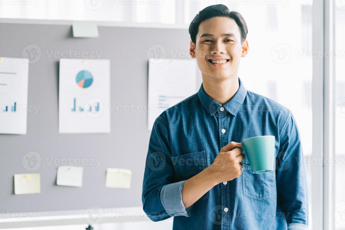 hombre asiático, tenencia, taza de café, posición, sonriente, con, planificación, tablero, plano de fondo foto