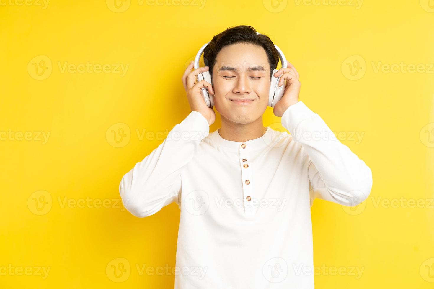 Foto de hombre asiático con camisa blanca escuchando música con los ojos cerrados sobre fondo amarillo